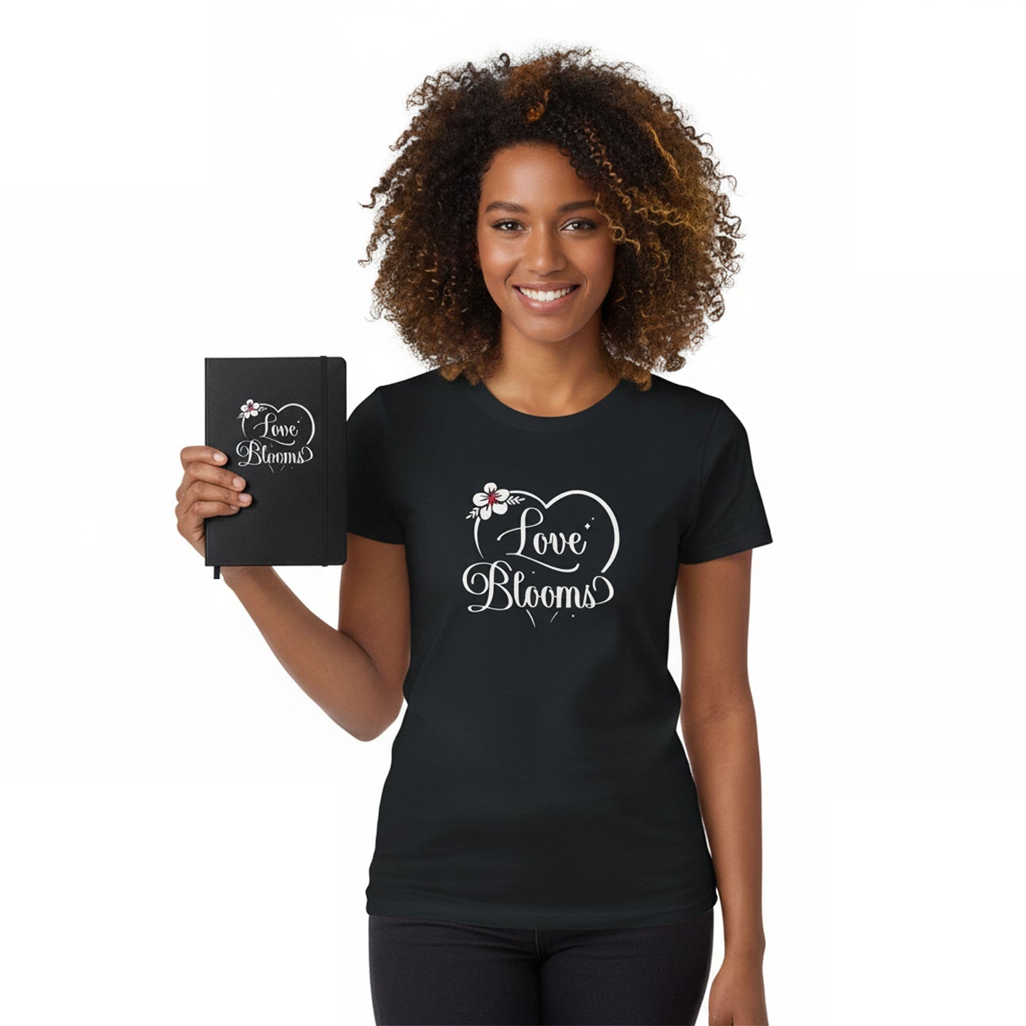 Woman wearing a black t-shirt with 'Love Blooms' design, holding a matching notebook.