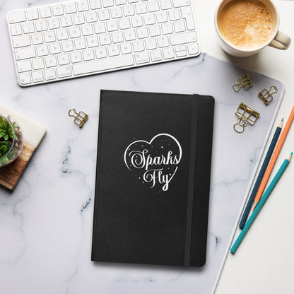 Black hardcover Sparks Fly Heart notebook on a desk.
