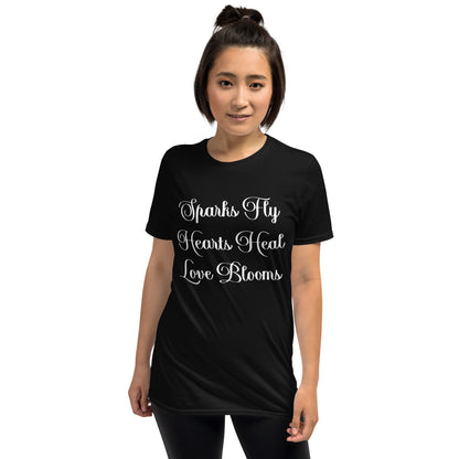 Woman wearing black Love's Journey Words t-shirt. Has the words Sparks Fly, Hearts Heal, Love Blooms.